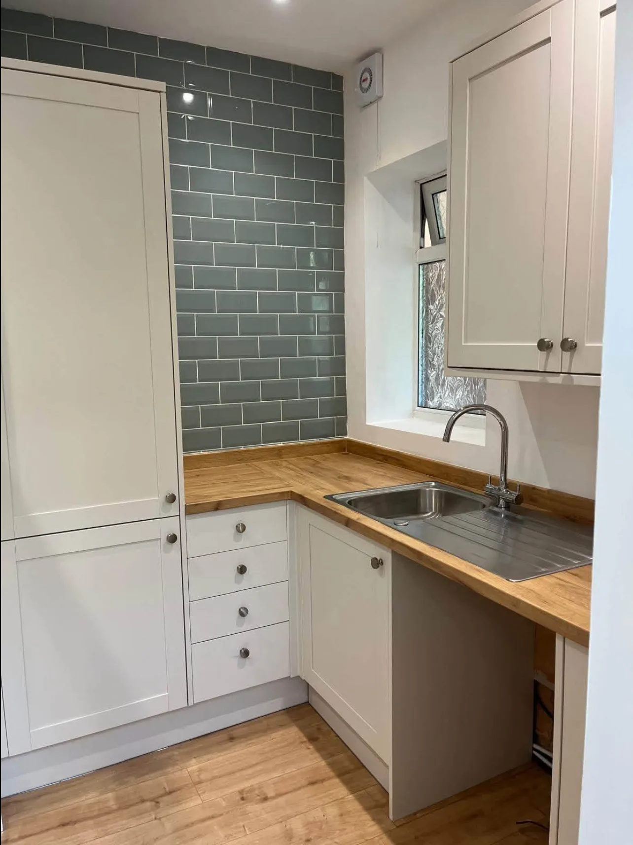 After: the finished Parkstone kitchen with cream shaker units, solid oak worktops, a new sink and green metro tiling