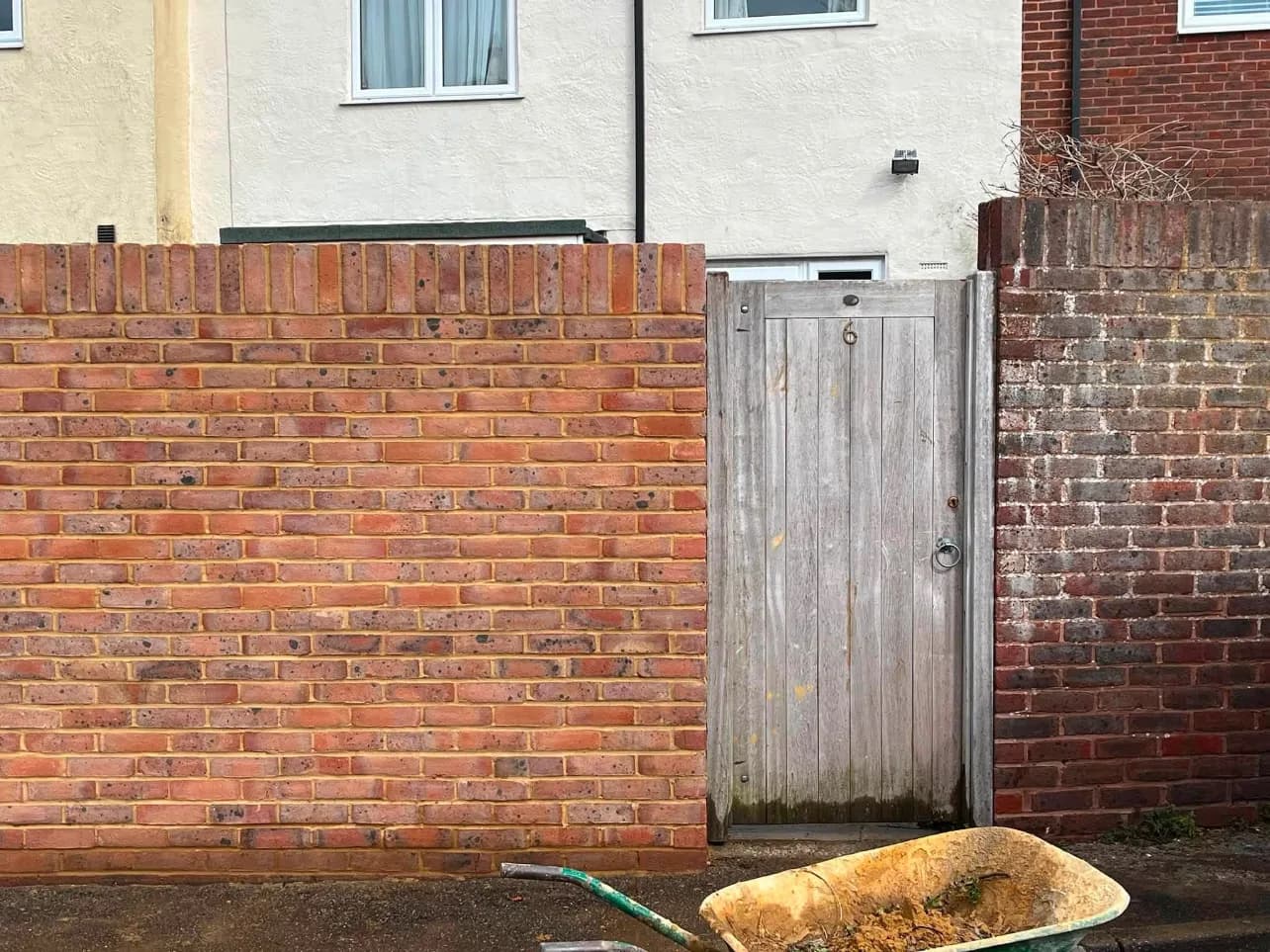A newly built brick boundary wall running up to a timber gateway, with the ground cleared and levelled in front of it