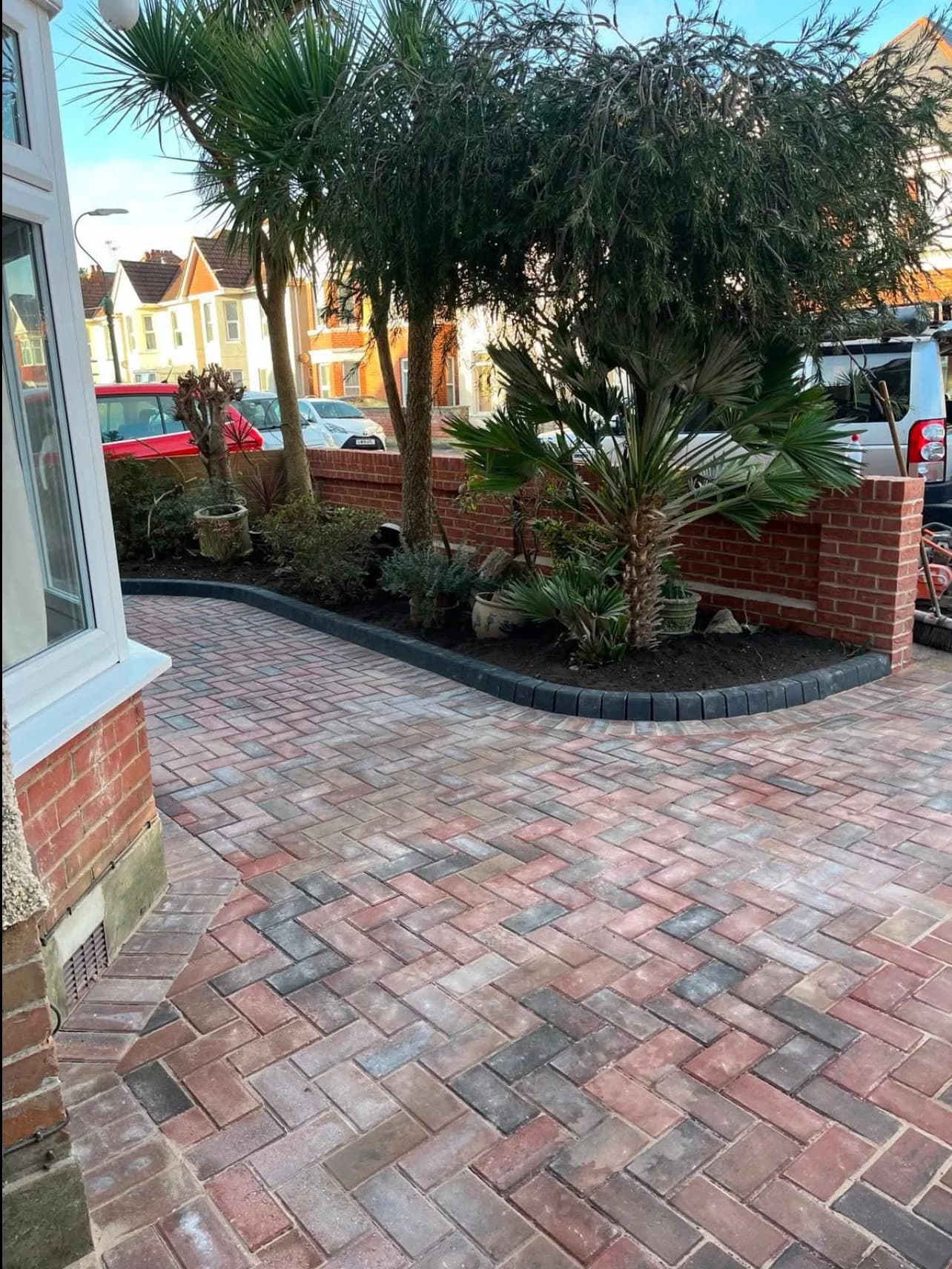 The completed Charminster frontage: block paving laid in herringbone with a kerbed edge, planted border and the new brick wall behind