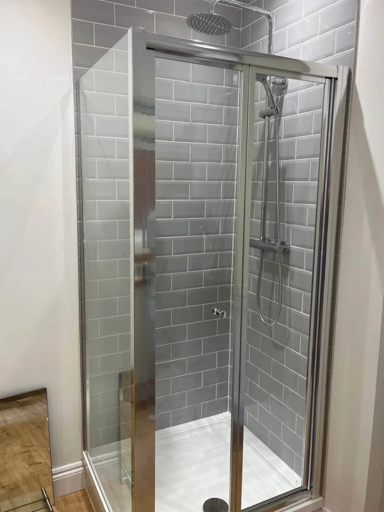 A completed shower room with a rainfall shower, grey metro tiling, a low-profile tray and oak-effect flooring